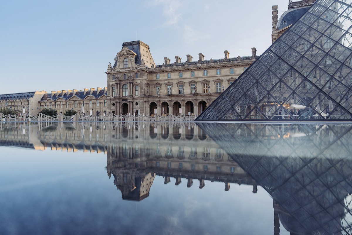 The Louvre and its glass pyramid reflected in still water, Paris